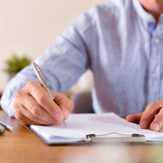 Man filling out a questionnaire on a wooden table. Horizontal composition. Front view.